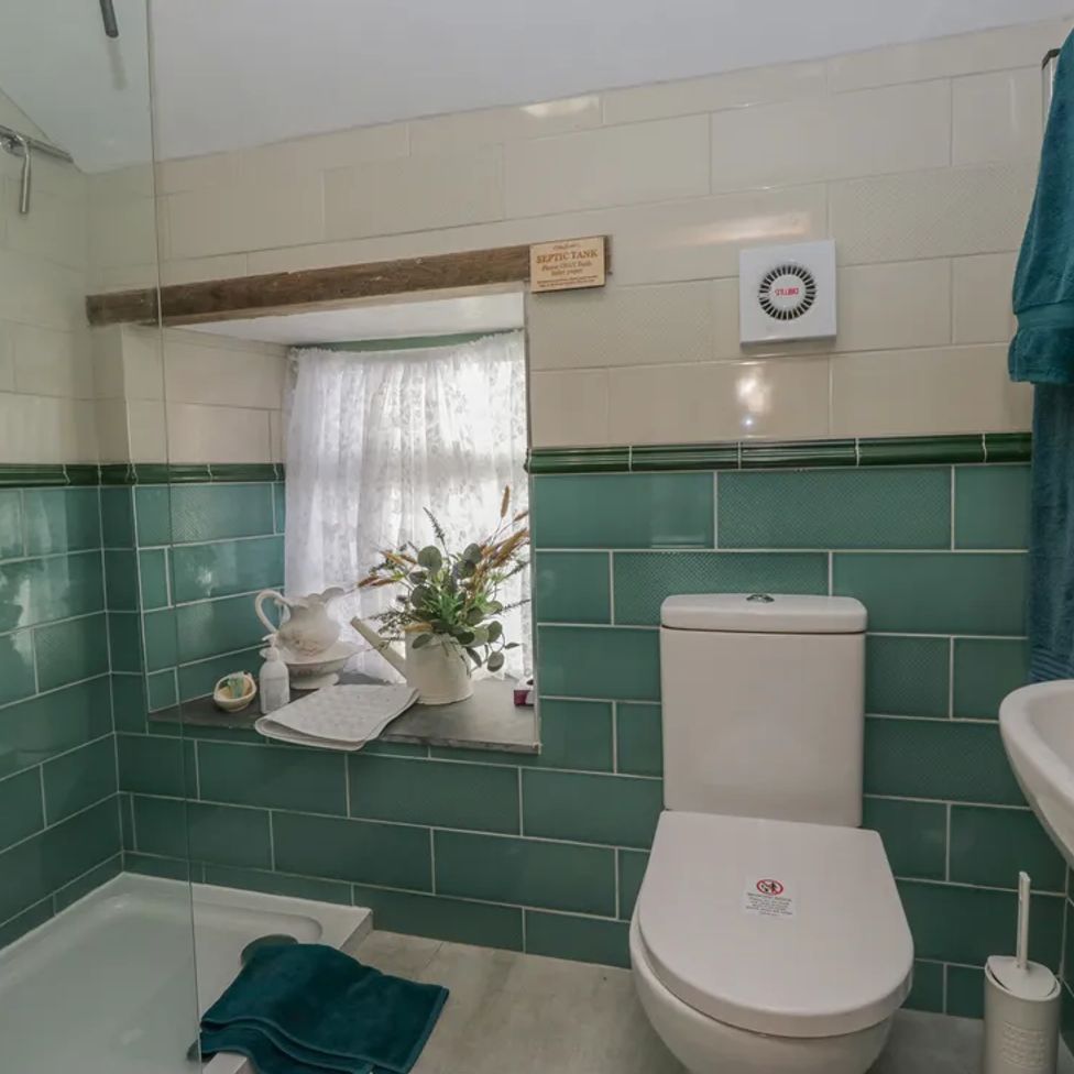 A bathroom with a toilet sink shower and window with flowers on the ledge at The Old Cart House in Garsdale near Sedbergh