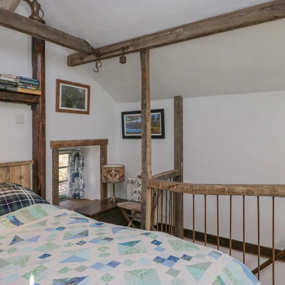 A bedroom with a bed a bookshelf lamp framed pictures and wooden beams at The Old Cart House in Garsdale near Sedbergh