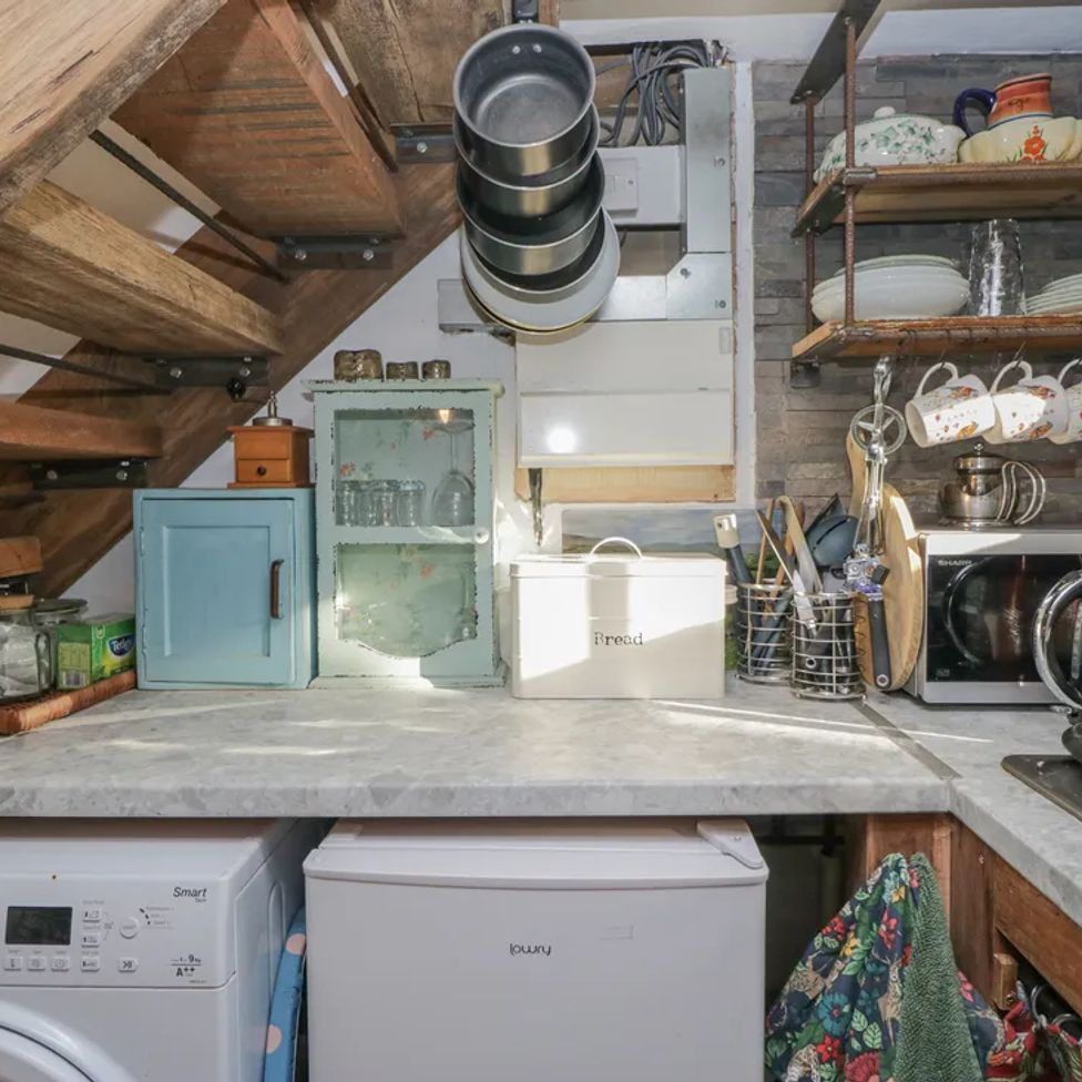 A kitchen corner with a countertop holding a small blue cabinet glassware bread box microwave red kettle and hanging pans and cups at The Old Cart House in Garsdale near Sedbergh