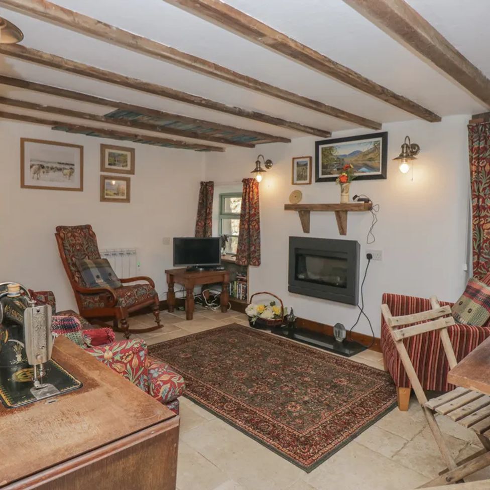 A living room with wooden beams floral and striped chairs a rug a sewing machine and a TV at The Old Cart House in Garsdale near Sedbergh