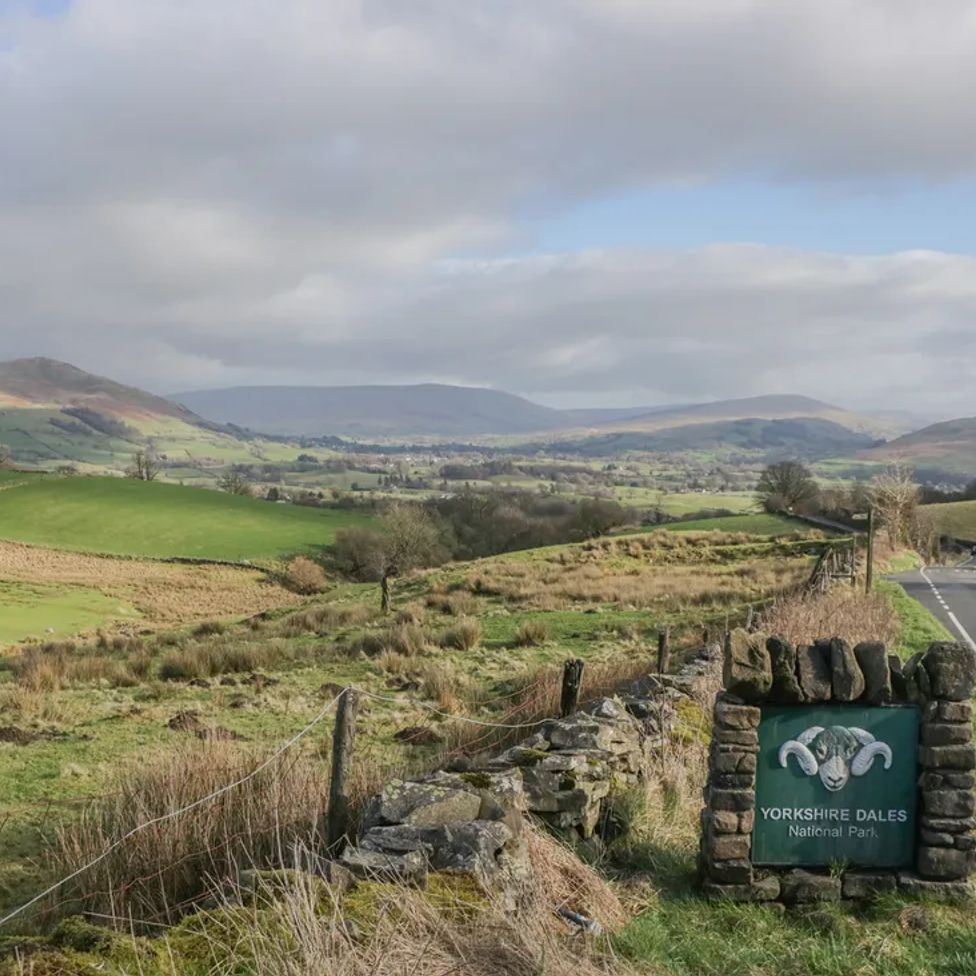 A road with a Yorkshire Dales National Park sign and fields and hills in the background at The Old Cart House in Garsdale near Sedbergh