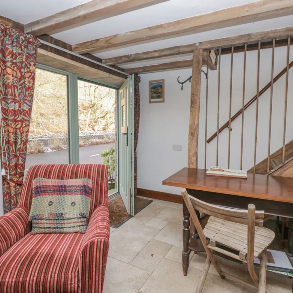 A room with a red striped armchair near an open door and wooden table with chairs under a staircase at The Old Cart House in Garsdale near Sedbergh