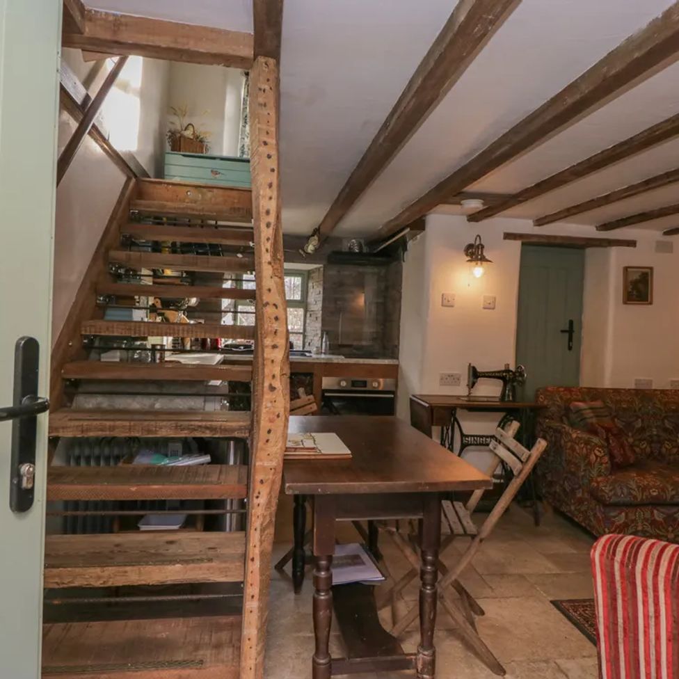 A rustic living area with wooden staircase, dining table with chairs, floral sofa, and vintage sewing machine at The Old Cart House in Garsdale near Sedbergh