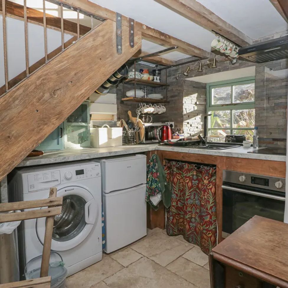 A small kitchen with a washing machine fridge oven wooden stairs and window at The Old Cart House in Garsdale near Sedbergh