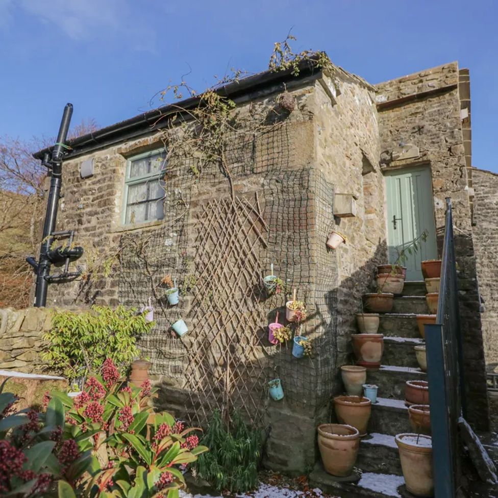 A stone house with a staircase lined with plant pots and a green door at The Old Cart House in Garsdale near Sedbergh