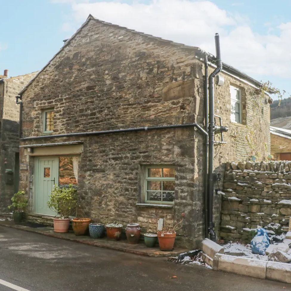 A stone house with potted plants outside and a stone wall with snow at The Old Cart House in Garsdale near Sedbergh