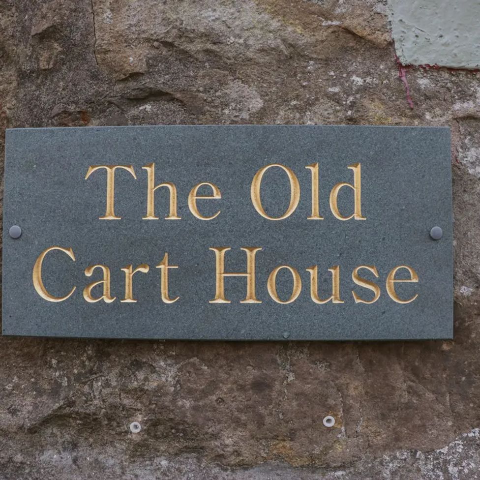 A stone wall with a rectangular plaque that says The Old Cart House