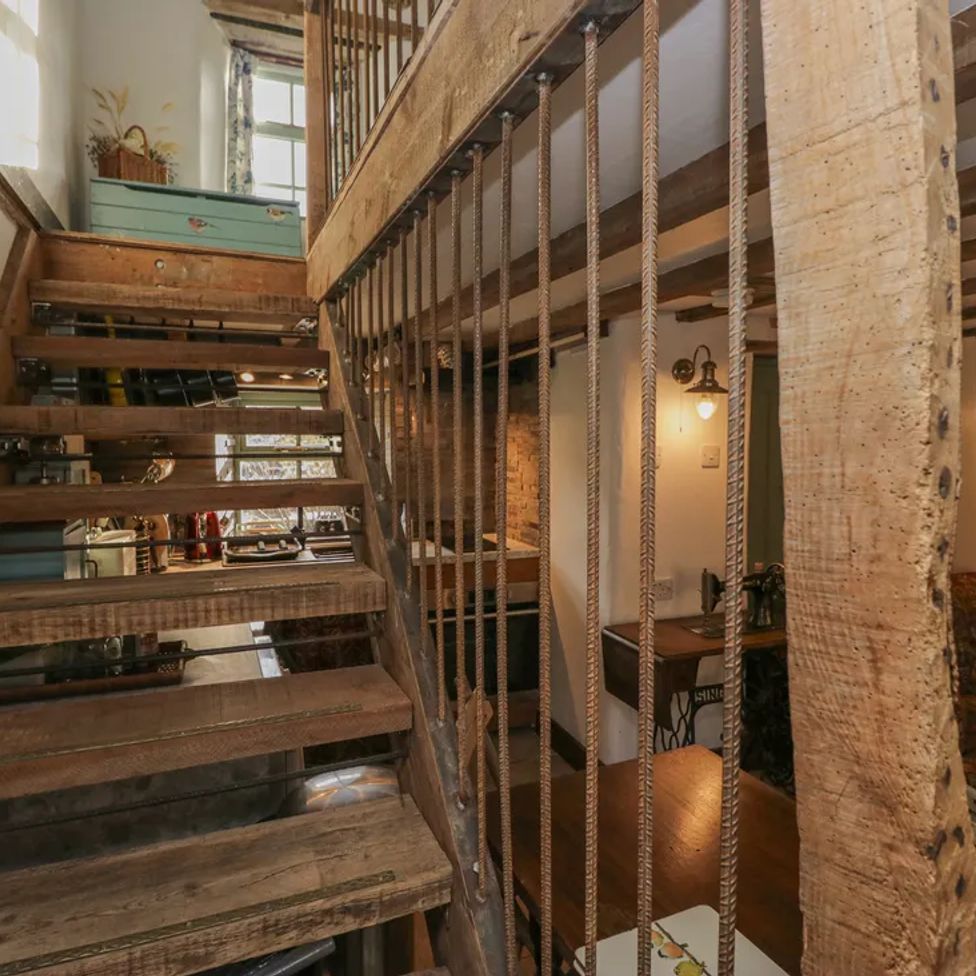 A wooden staircase with metal railings inside a room with a small dining area and a sofa at The Old Cart House in Garsdale near Sedbergh