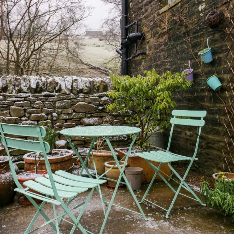 An outdoor patio with two mint green chairs and a round table near a stone wall with potted plants at The Old Cart House in Garsdale near Sedbergh