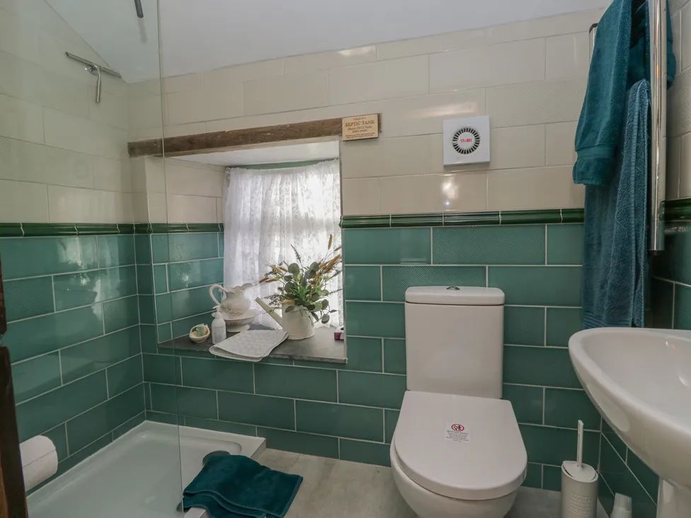 A bathroom with a toilet sink shower and window with flowers on the ledge at The Old Cart House in Garsdale near Sedbergh