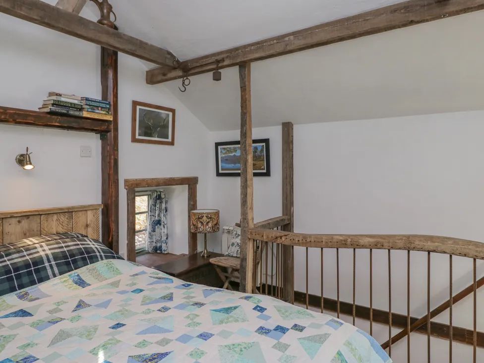 A bedroom with a bed a bookshelf lamp framed pictures and wooden beams at The Old Cart House in Garsdale near Sedbergh