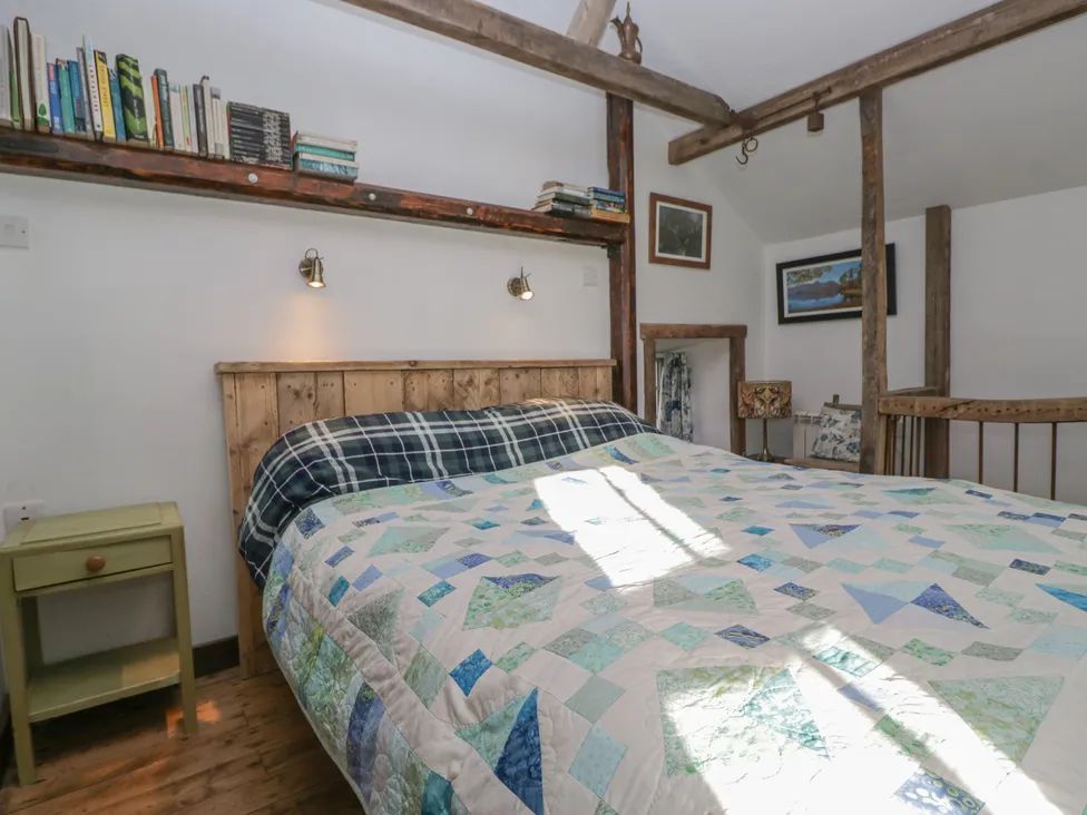 A bedroom with a wooden bed frame quilted bedspread green bedside table books on a wall shelf and framed pictures at The Old Cart House in Garsdale near Sedbergh