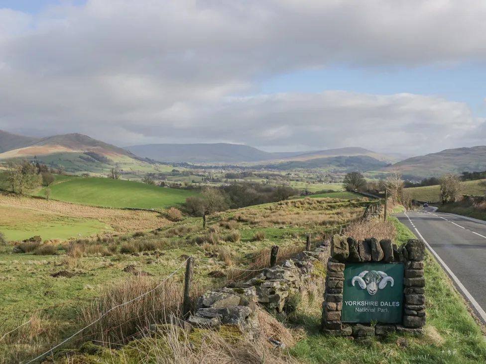 A road with a Yorkshire Dales National Park sign and fields and hills in the background at The Old Cart House in Garsdale near Sedbergh
