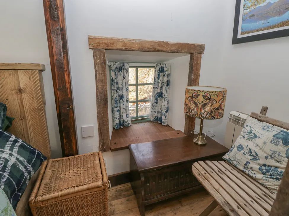 A small seating area with a wooden chair a wicker basket a wooden table and a window with curtains at The Old Cart House in Garsdale near Sedbergh