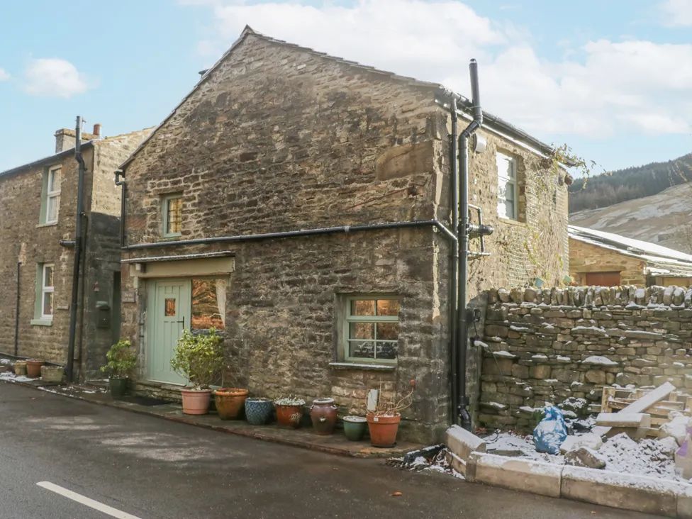 A stone house with potted plants outside and a stone wall with snow at The Old Cart House in Garsdale near Sedbergh