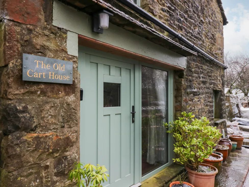 The exterior entrance of a stone house with a green door and multiple potted plants at The Old Cart House in Garsdale near Sedbergh