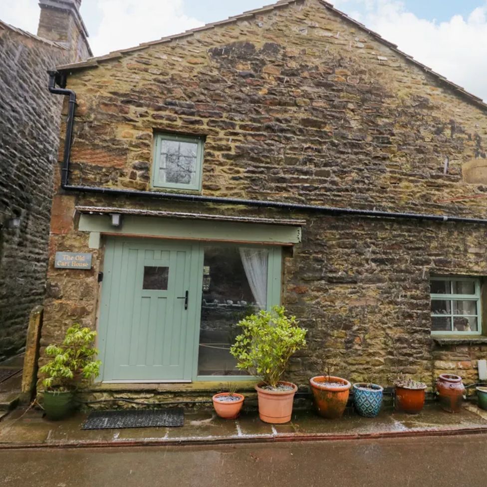 Stone exterior of a house with green door and windows and potted plants outside at The Old Cart House in Garsdale near Sedbergh