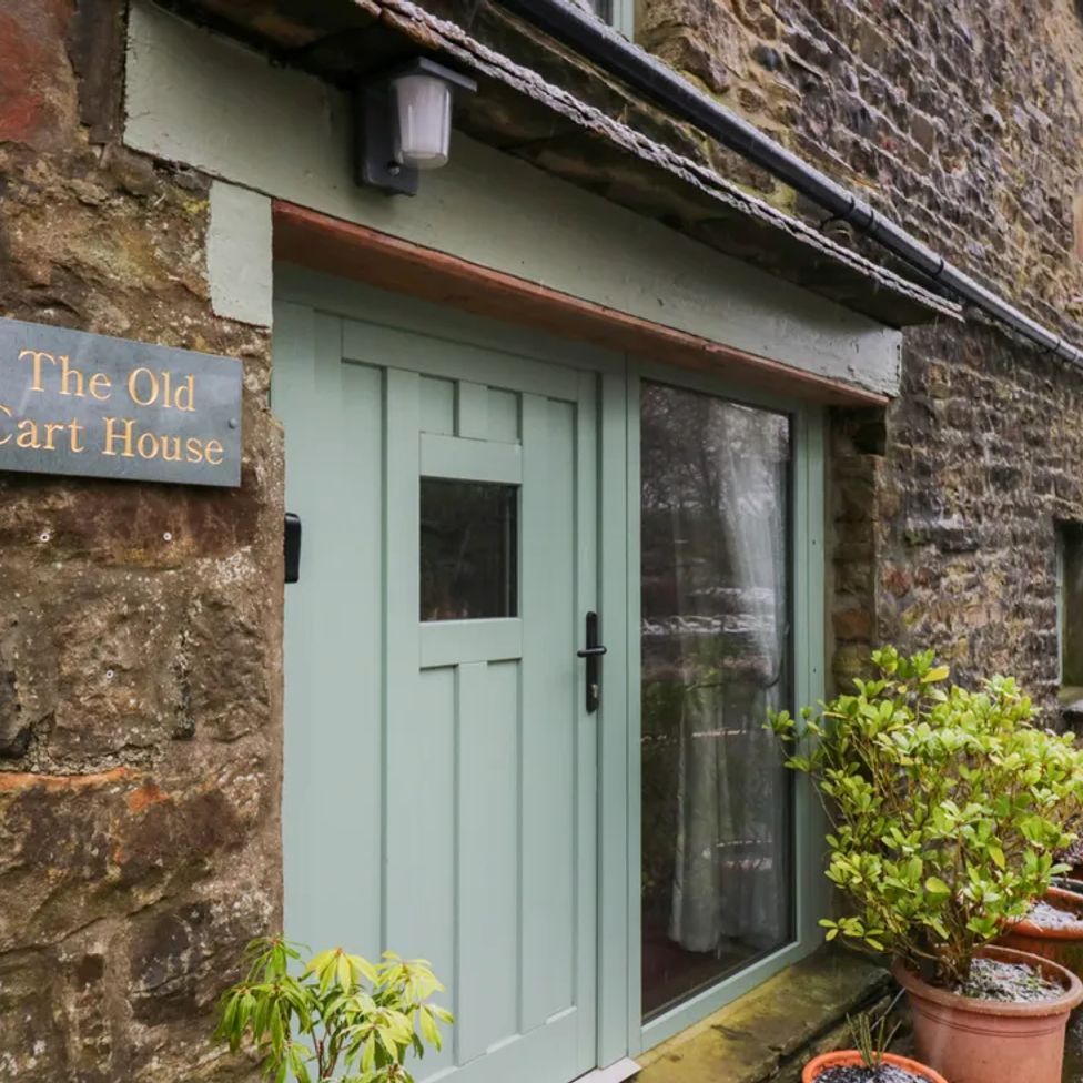 The exterior entrance of a stone house with a green door and multiple potted plants at The Old Cart House in Garsdale near Sedbergh
